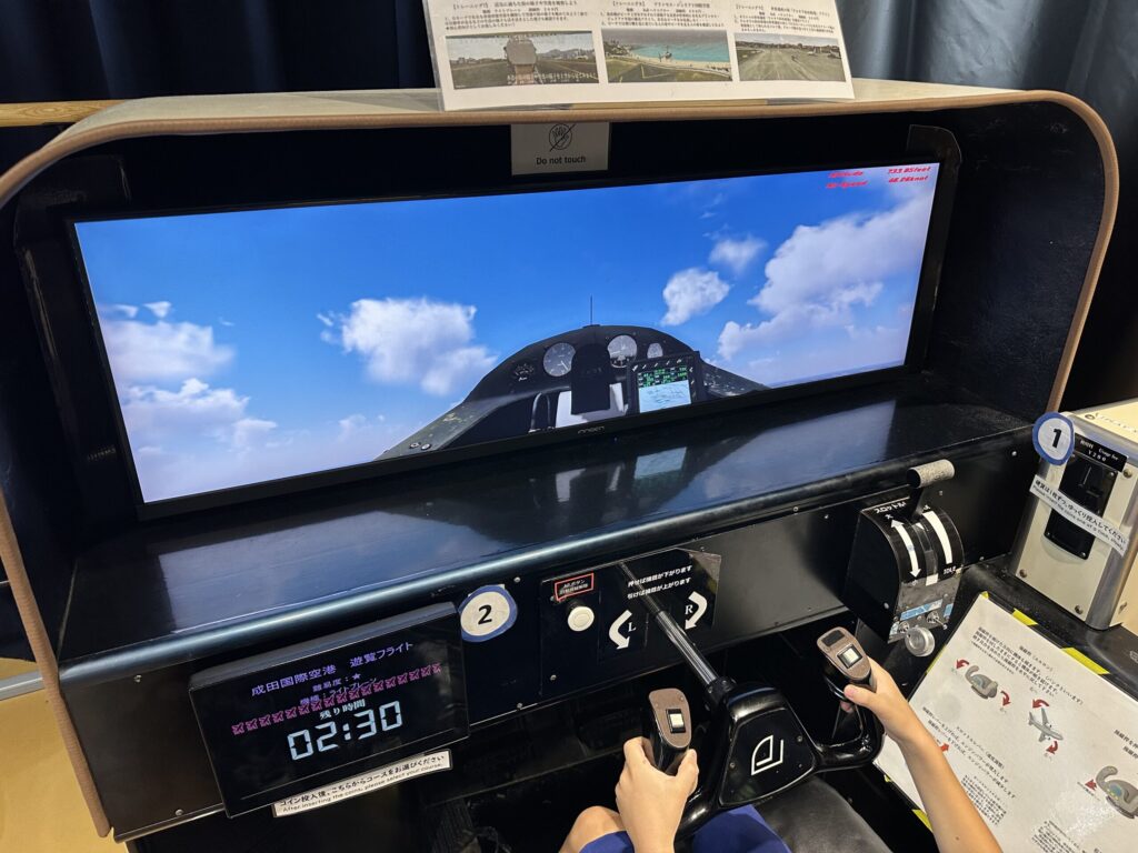 子どもが操縦桿を握って遊覧フライトのシミュレーターを操作する様子