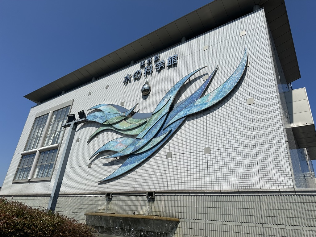 東京都水の科学館の外壁にある水色の波のオブジェと館名看板