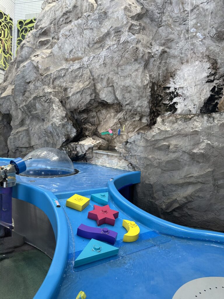 アクアパークの岩場を模した壁と星や月のボタンが付いた水遊び台