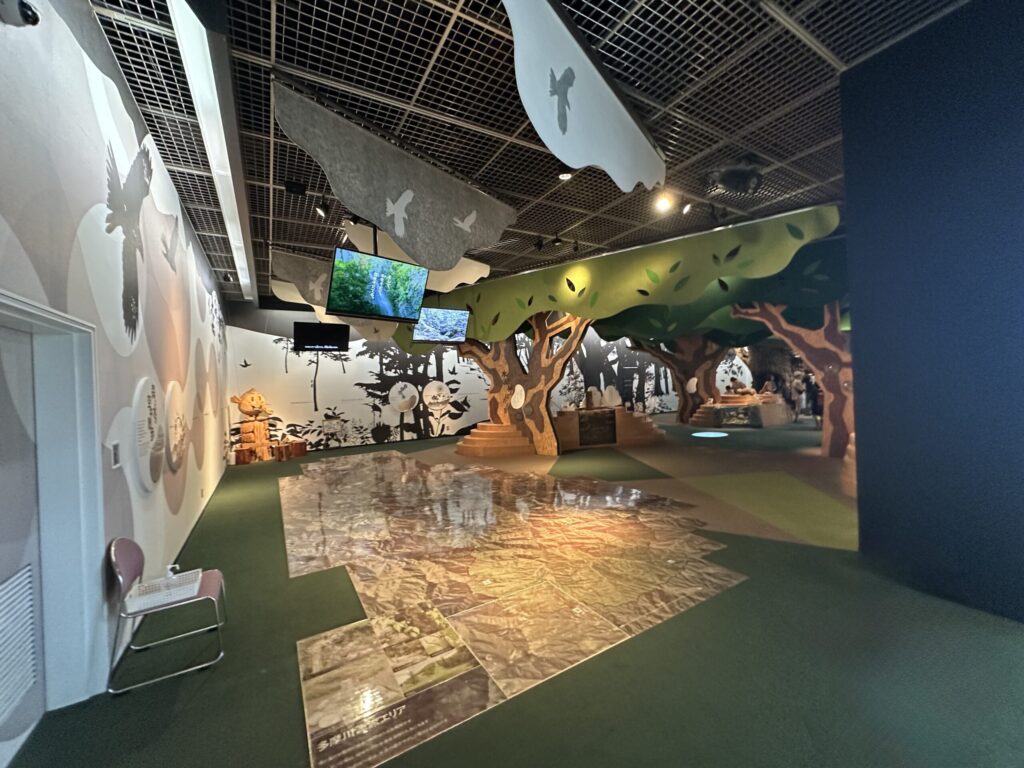木々の装飾と床の航空地図が広がるアクアフォレストの展示エリア