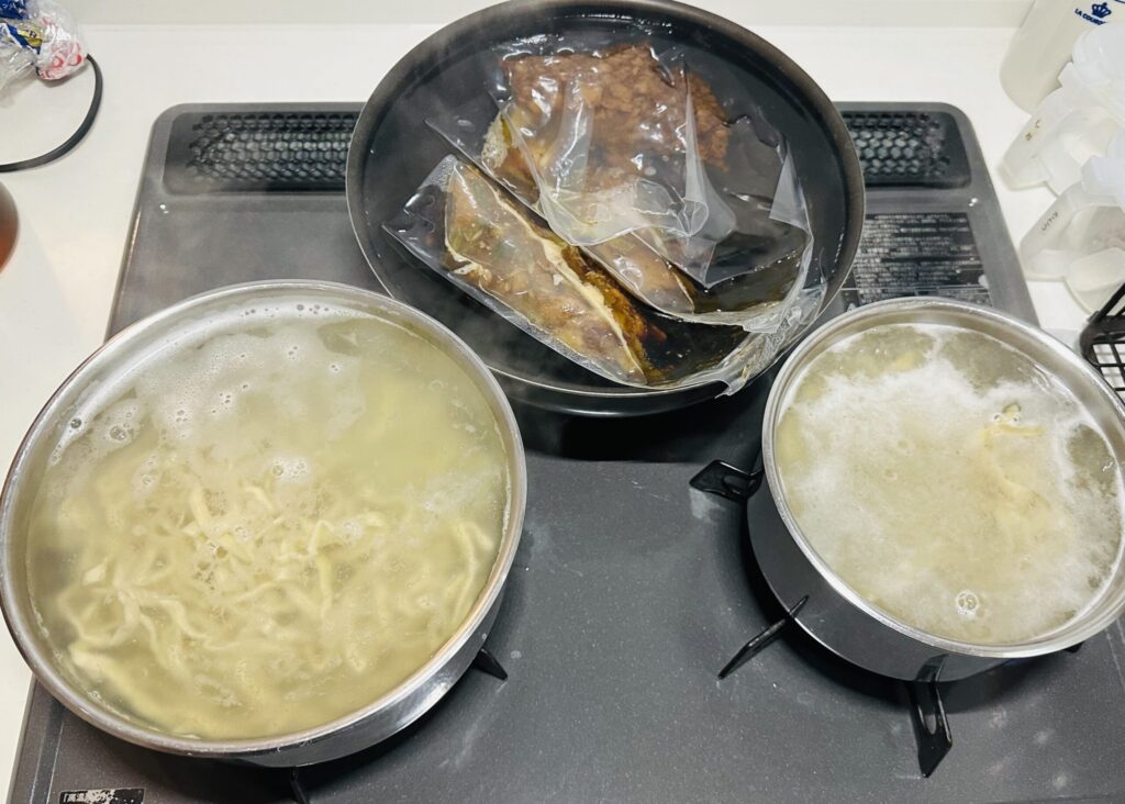 鍋2つで麺を茹でながらスープと具材のパックを湯煎する様子
