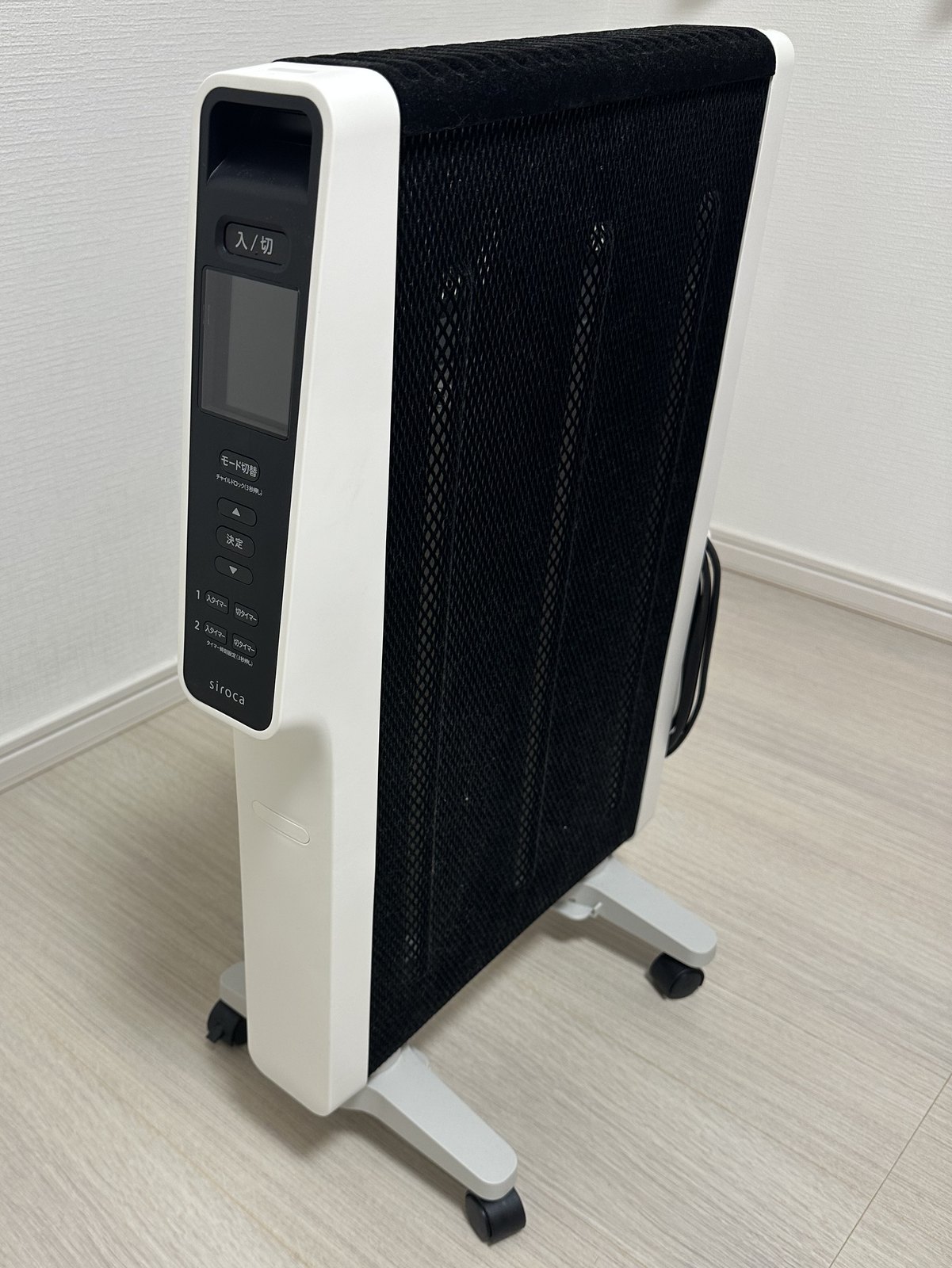 シロカの遠赤軽量ヒーター かるポカ SN-M371を、脚を開いて床に置いたところ。細い面に操作パネルがあり、広い面は黒い網目になっている